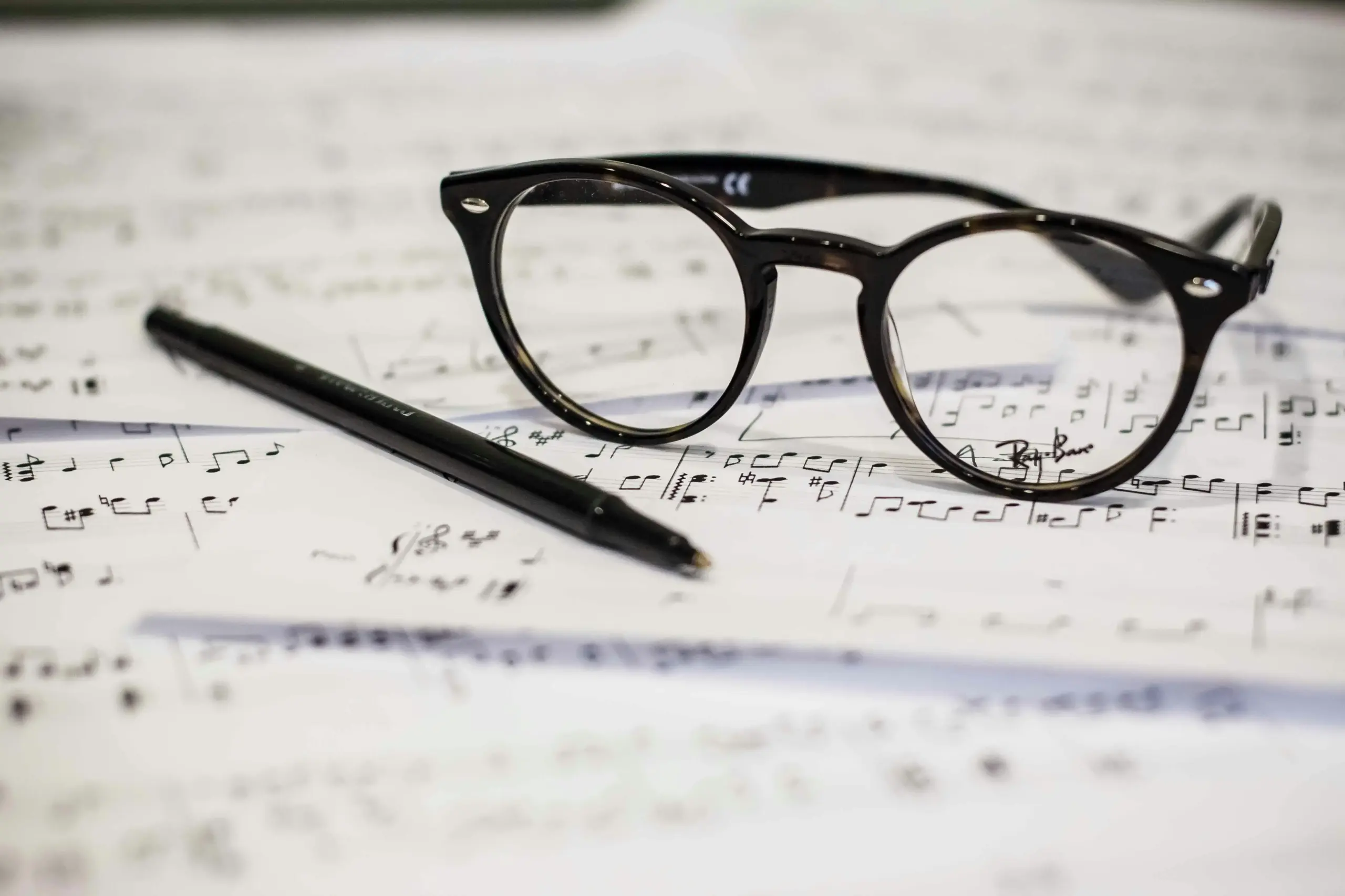 Sheet music with glasses and a pen on a dark surface, symbolizing research and performance studies